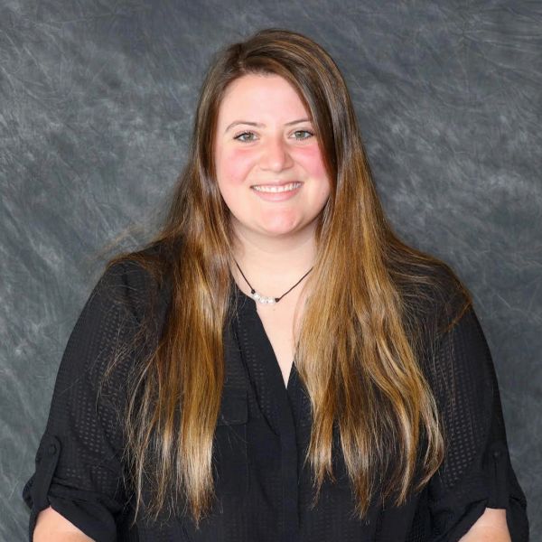 Smiling woman with long light brown hair in a black shirt against a gray backdrop.