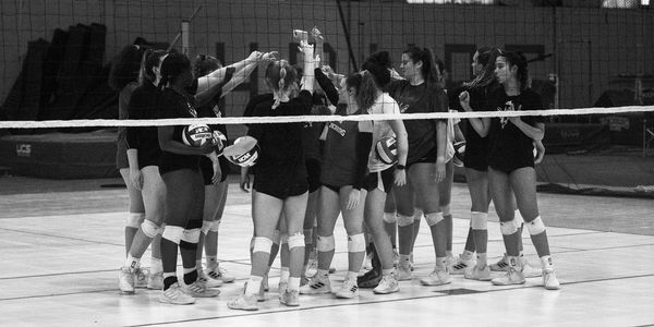 Women volleyball team huddling before a game in gym.