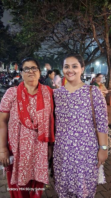Two women smiling outdoors at night, dressed in traditional attire.