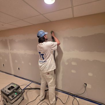 Man sanding drywall in a room under renovation.