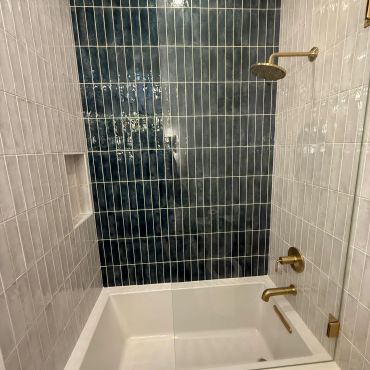 Modern bathtub with dark blue and light tiles and gold fixtures.