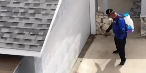 Person spraying exterior wall with backpack sprayer.