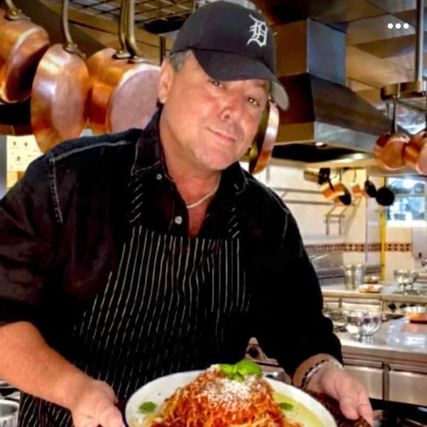 Chef presenting a plate of spaghetti in a professional kitchen.