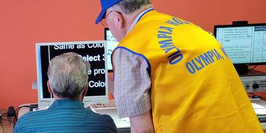 Lion in bright yellow vest shows low vision client at the Low Vision Resource Center how to use CCTV