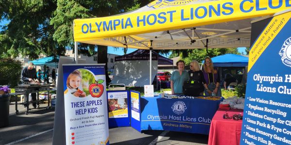 A man grilling hotdogs and three women hosting an info table at an event