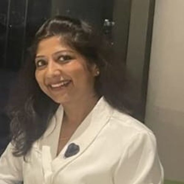 Smiling woman with long dark hair wearing a white shirt indoors.