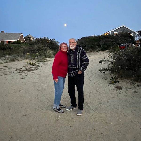 A photograph of a mature couple on a beach with a full moon in the background.