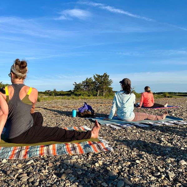 A photograph of women doing a seated yoga pose on a beach.