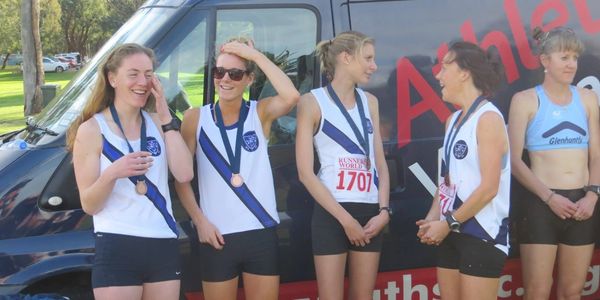4 MUAC athletes at a cross country meet, each wearing a medal, smiling and interacting