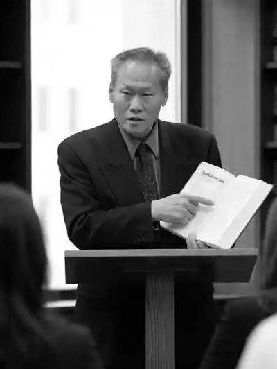 Man in suit reading from a book at a podium.