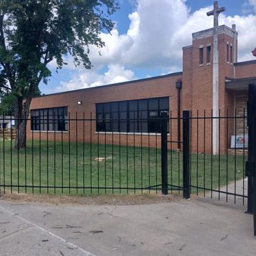 Brick building with a cross and black metal fence under a blue sky.
