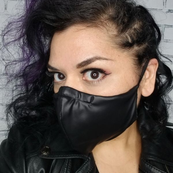 Person with dark curly hair wearing a black face mask and leather jacket.