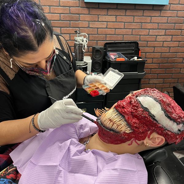 Artist applying detailed makeup effects to create a monster face with sharp teeth.
