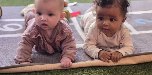 Two babies lying on a mat, looking curious and engaged.