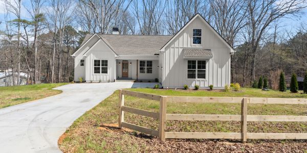 Modern farmhouse with white exterior and wooden fence on a sunny day.