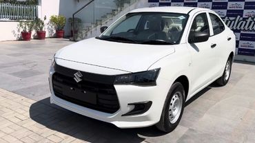 White Suzuki sedan parked outdoors near a showroom.