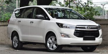 White Toyota Innova parked near a tree in an outdoor setting.