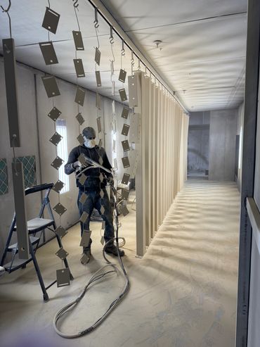 Worker spray painting metal pieces in a well-lit industrial room.