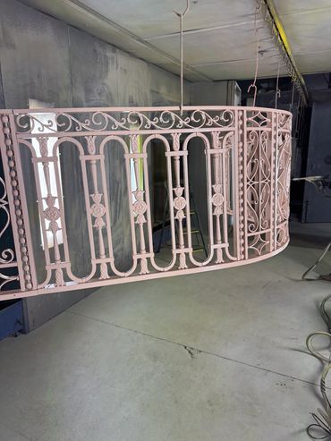 An ornate metal railing painted in light pink, hanging in an industrial space.