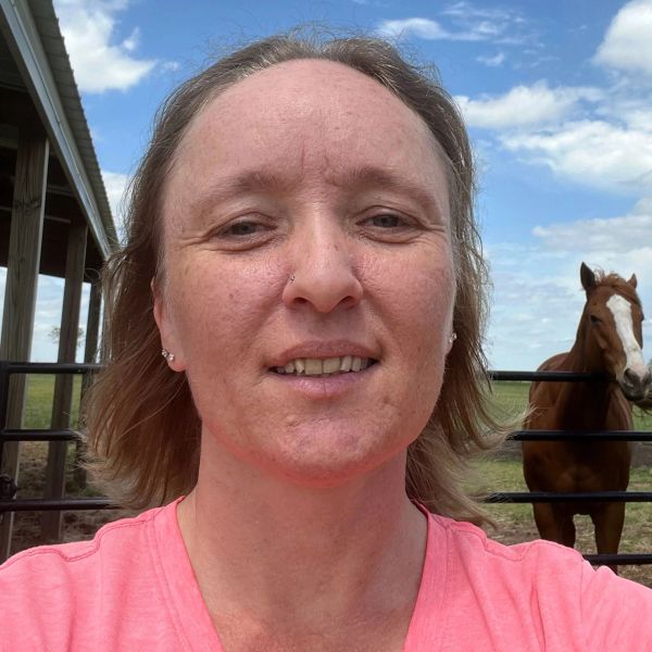 Woman taking a selfie outdoors with a horse in the background.