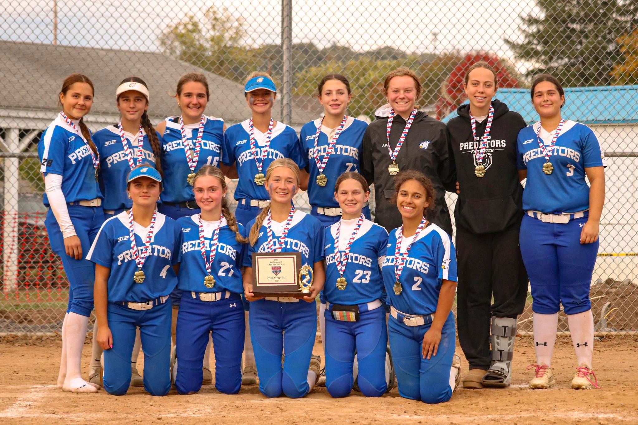 A girls softball team posing with medals and a championship plaque.
