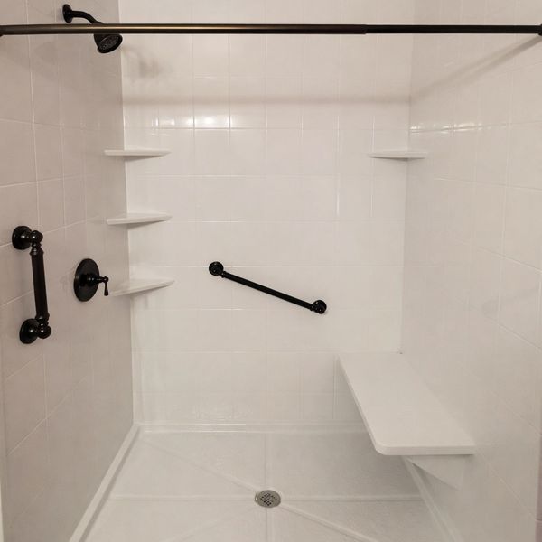 A clean white tiled shower with black fixtures and a built-in bench improving accessibility