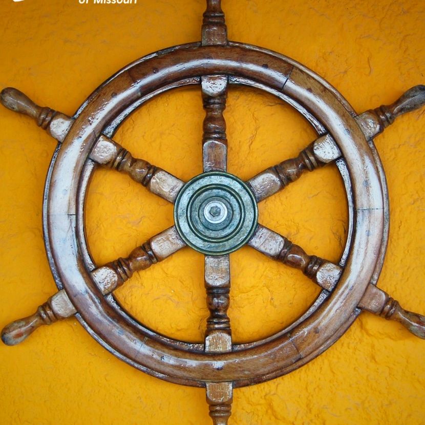 Wooden ship wheel on yellow wall symbolizing guidance and trauma-informed therapy in Missouri.