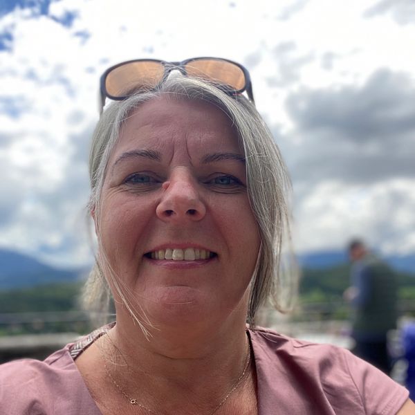 Smiling woman with sunglasses on her head outdoors under cloudy sky.