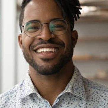 Smiling man with glasses and patterned shirt indoors.