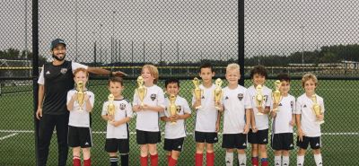 Youth soccer team with trophies and coach on field.