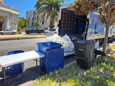 Moving truck with recycling bins and packing materials on a sunny street.