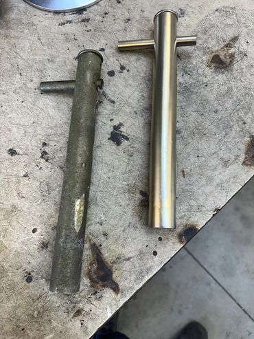 Two metal pipe fittings, one old and rusty, one new and shiny, on a scratched workbench.
