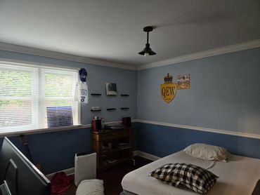 A bedroom with light blue walls, a twin bed with a checkered pillow, and a window with blinds