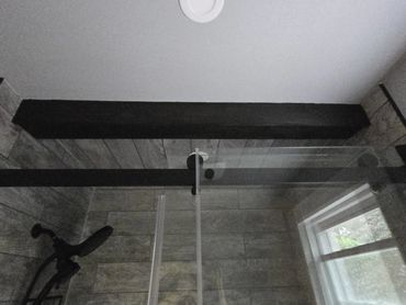 Modern shower with a matte black dual showerhead against gray wood-look tiled walls and ceiling