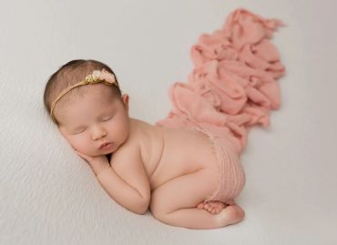 Sleeping baby girl wearing a pink headband and diaper cover.