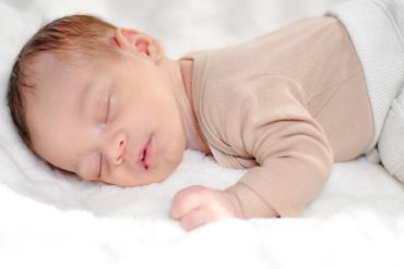 Sleeping newborn baby lying on a soft white blanket.