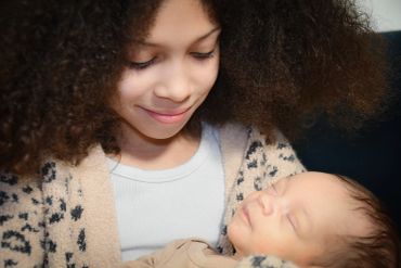 Girl smiling at sleeping baby.