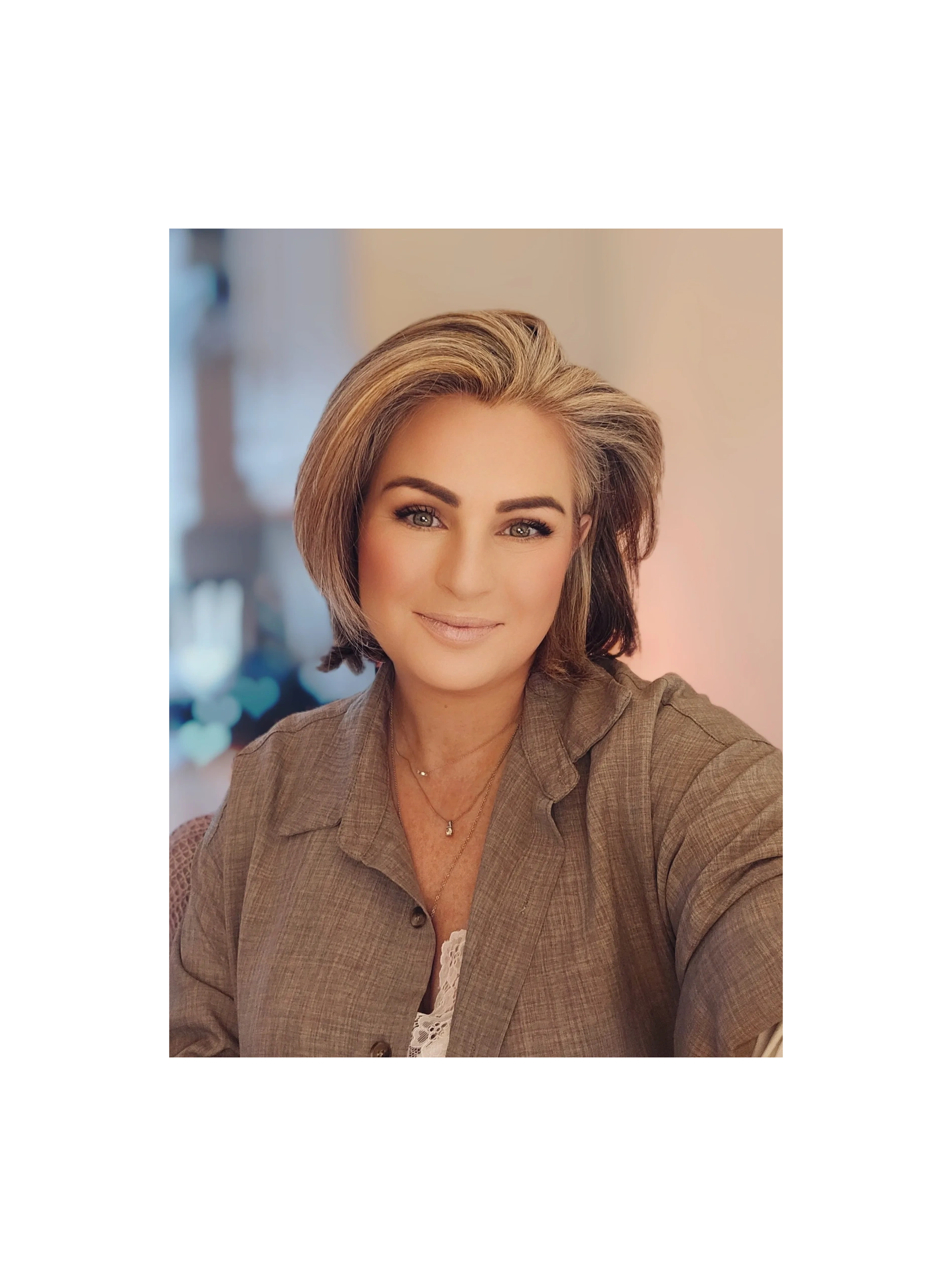 Smiling woman with short hair wearing a brown shirt and gold necklaces.