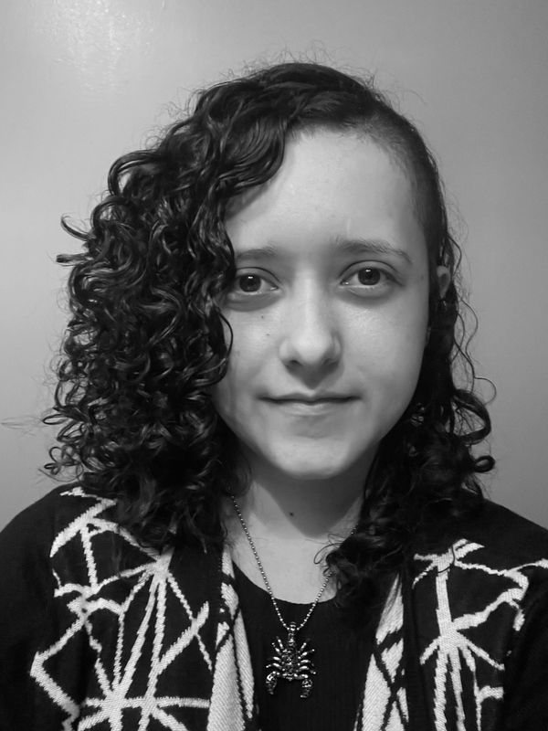 Black and white portrait of a person with curly hair and a spider necklace.
