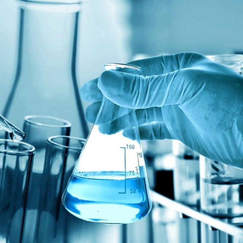 Gloved hand holding a flask with blue liquid in a laboratory setting.