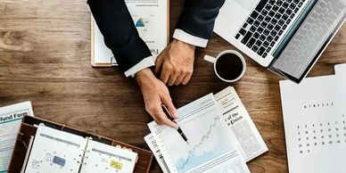 Businessman analyzing financial charts and calendar at a wooden desk with coffee and laptop.
