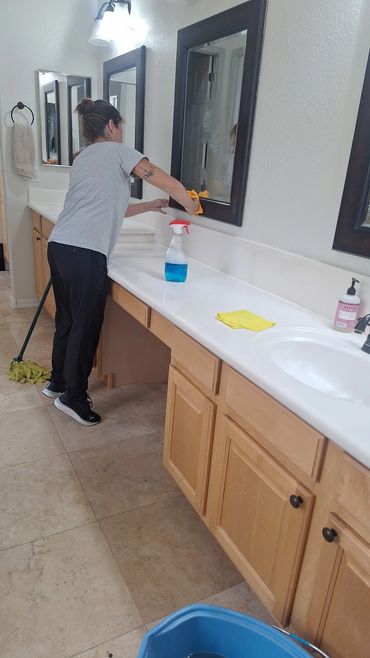 Person cleaning a bathroom mirror with a cloth and spray bottle.