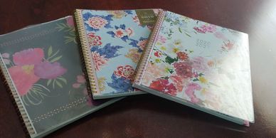 Three floral-covered planners on a brown surface.