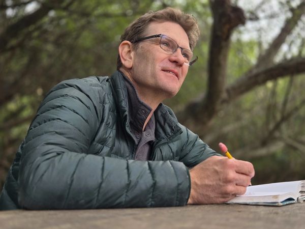 Man in jacket writing in a notebook outdoors.
