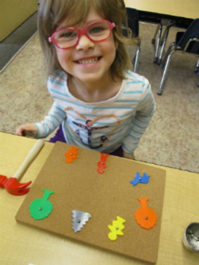 little girl pinning cut out shapes on corkboard