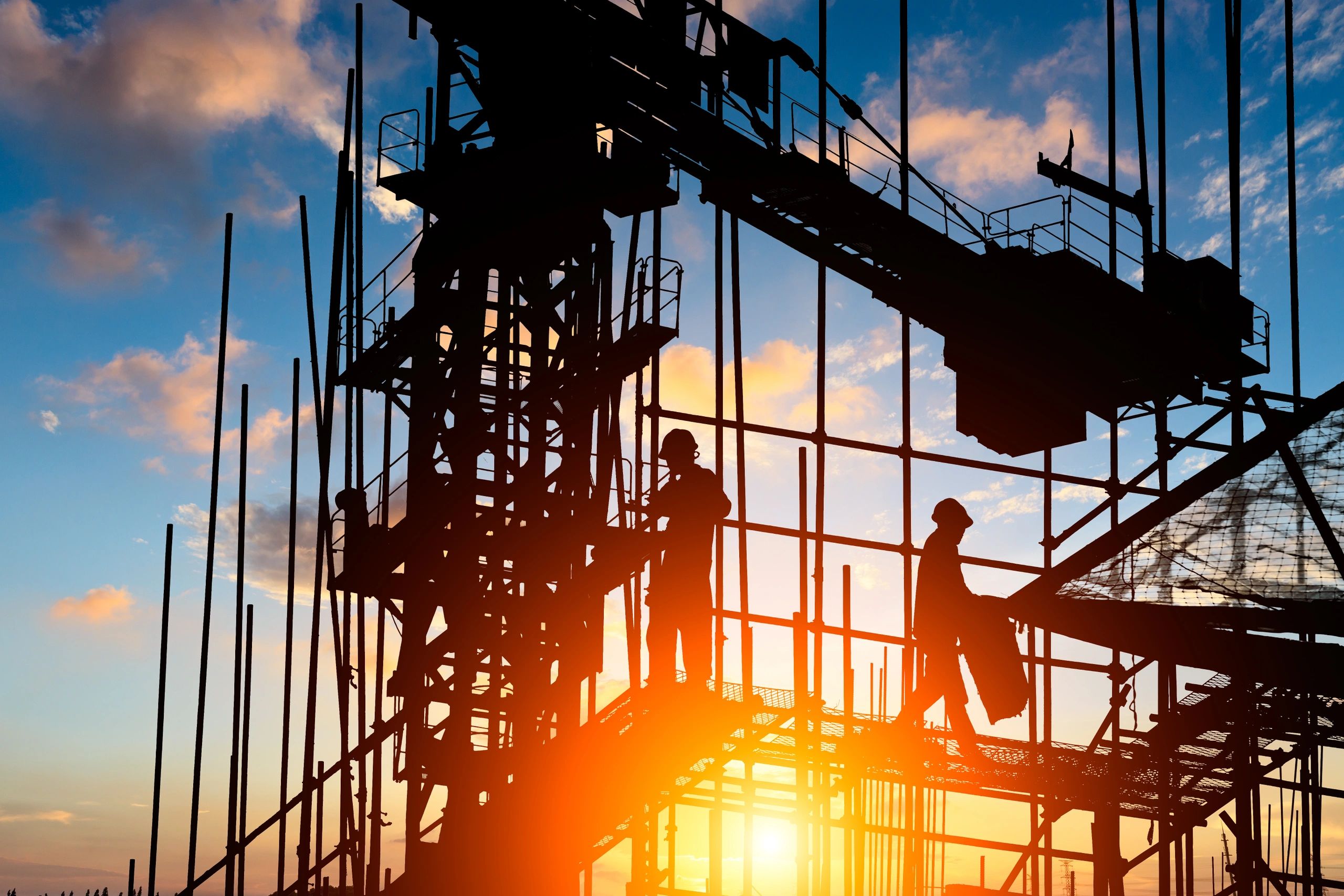 Silhouettes of construction workers on scaffolding during sunset.