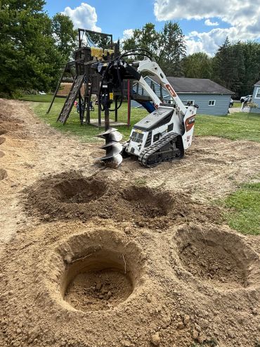 Mini excavator drilling holes in soil.