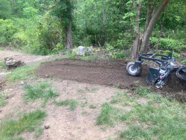 Freshly tilled soil with surrounding trees and a machine attachment.