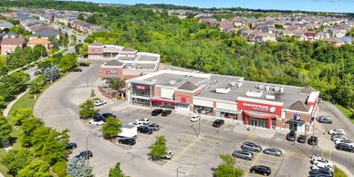 A suburban shopping plaza with stores and parking spaces surrounded by greenery.