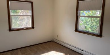 Empty corner room with two windows and beige carpet.